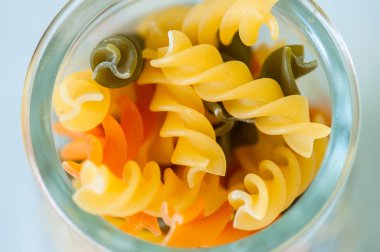 Bir cam kavanoza çiğ renkli makarna. Beyaz arka plan.