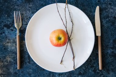 Mavi ston üzerinde beyaz tabak, Kırmızı elma, çatal bıçak takımı ve ağaç çorbaları