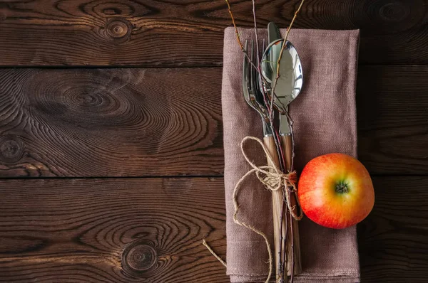 Ветви дерева, яблоко, столовые приборы на льняной мешковине на деревянной подстилке — стоковое фото