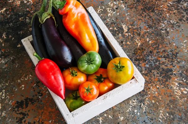 Witte doos met groenten op een roestig achtergrond. Aubergines, bel — Stockfoto