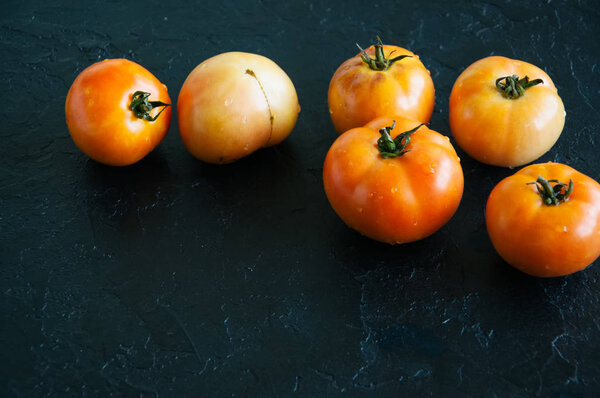 Orange fresh ripe tomatoes on a black stone background. Top view