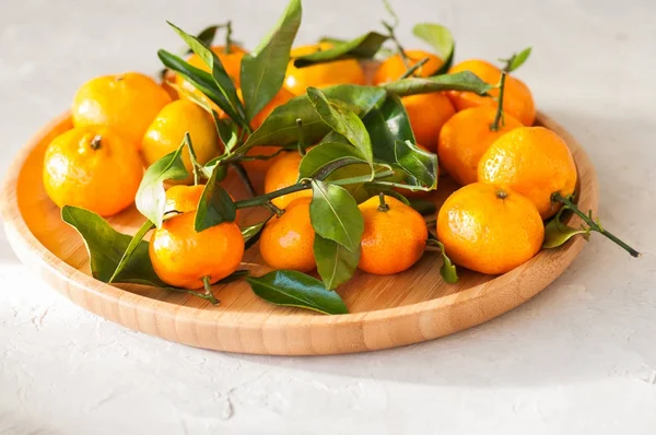Тарелка свежих и сочных мандаринов с листьями на белом камне — стоковое фото