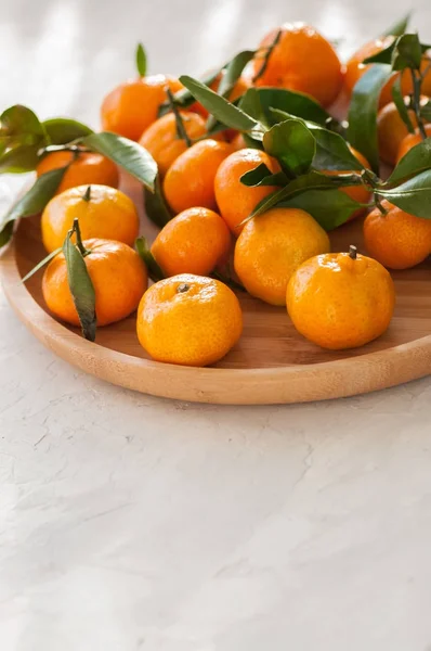 Тарелка свежих и сочных мандаринов с листьями на белом камне — стоковое фото