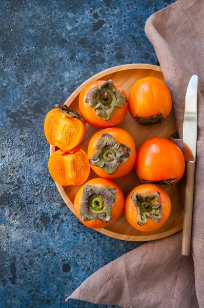 Fresh ripe persimmons on a wooden plate on a blue stone backgrou — Stock Photo, Image