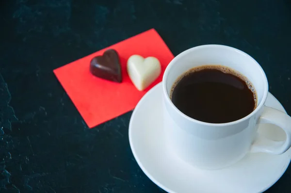 Tasse starken Kaffee und herzförmige dunkle und weiße Pralinen — Stockfoto