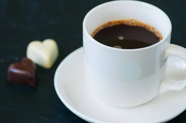 Copo de café forte e chocolates escuros e brancos em forma de coração — Fotografia de Stock