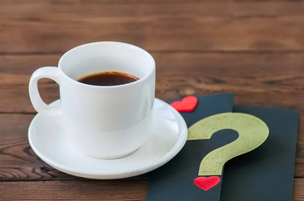 Uma xícara de café preto e um cartão em um fundo de madeira . — Fotografia de Stock