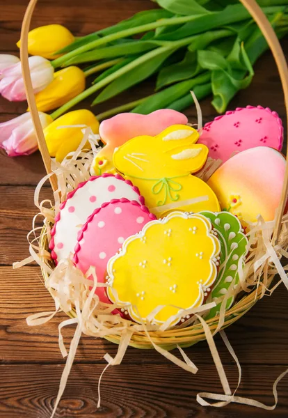 Bunte Osterhasen und Eierplätzchen in einem Korb auf einem Holztisch — Stockfoto