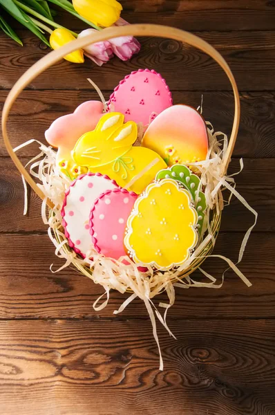 Bunte Osterhasen und Eierplätzchen in einem Korb auf einem Holztisch — Stockfoto