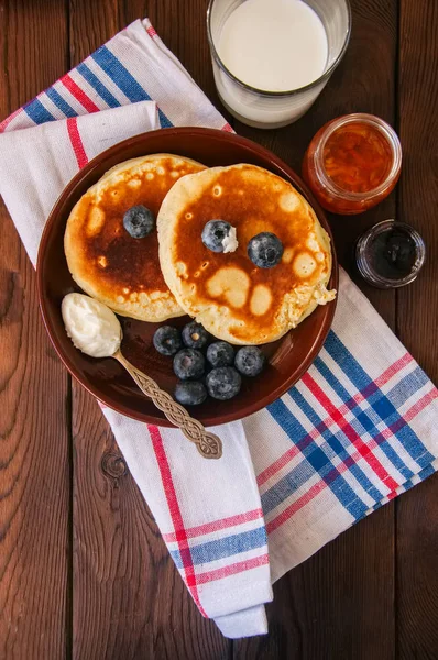 Pila de panqueques caseros con bayas en un plato, leche en una ja —  Fotos de Stock