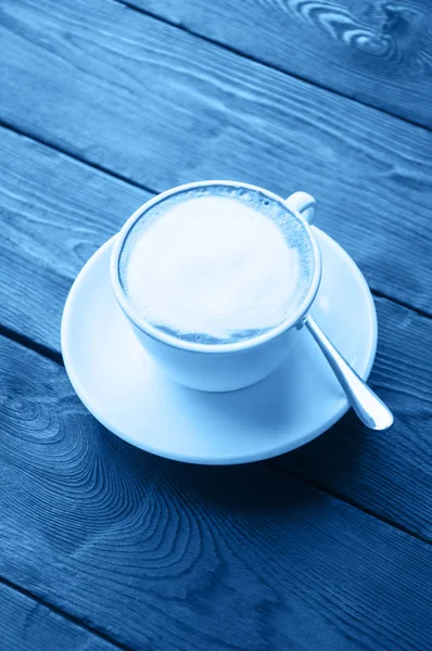 Uma xícara de latte em um fundo de madeira colorido na cor da moda azul — Fotografia de Stock