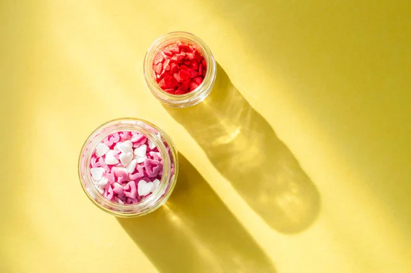 Heart shaped confetti in a glass jar on a bright yellow backgrou — Stockfoto