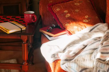 Evde kal, kitap oku ya da kendini izole et. Altın saat zamanı. Evin içi rahat. Kanepede kitap, masada bardak..