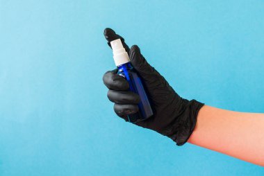 Elinde dezenfektan tutan siyah eldivenli bir el. Mavi arka plan. Güvenlik ya da sağlık koruma kavramı.