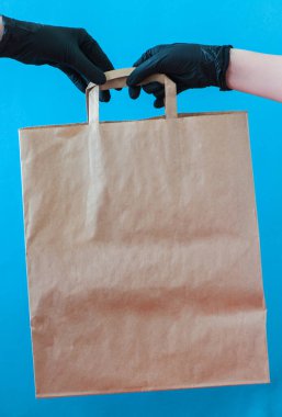 Siyah eldivenli kesilmiş eller mavi arka planda el işi kağıt torba tutuyor. Güvenlik servis konsepti. 