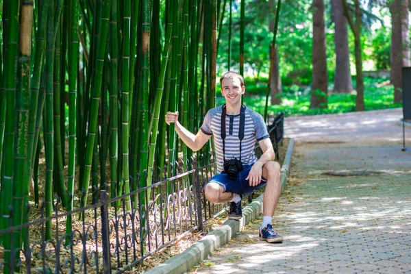 Fiatal és mosolygó ember, egy kamera áll közel a magas bambusz — Stock Fotó