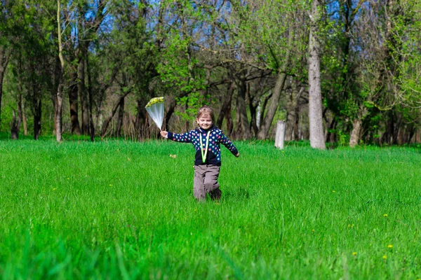 Маленька дівчинка стоїть на зеленій траві з пакетом квітів — стокове фото