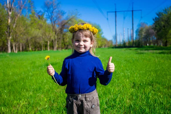 Маленькая девочка на зеленой траве с цветами и большим пальцем вверх — стоковое фото