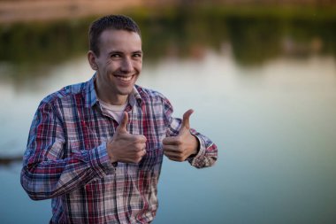 Genç bir adam baş parmakları nehir kıyısında oturur