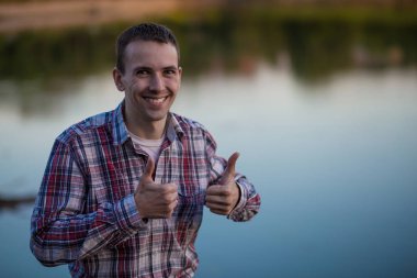 Genç bir adam baş parmakları nehir kıyısında oturur