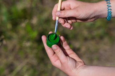 Bir kız bir yeşil boya ve fırça elinde tutuyor