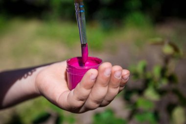 Bir çocuğun elinde pembe bir boya ve fırça tutuyor
