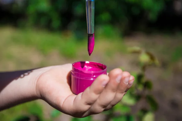 Un bambino tiene in mano una vernice rosa e un pennello — Foto Stock