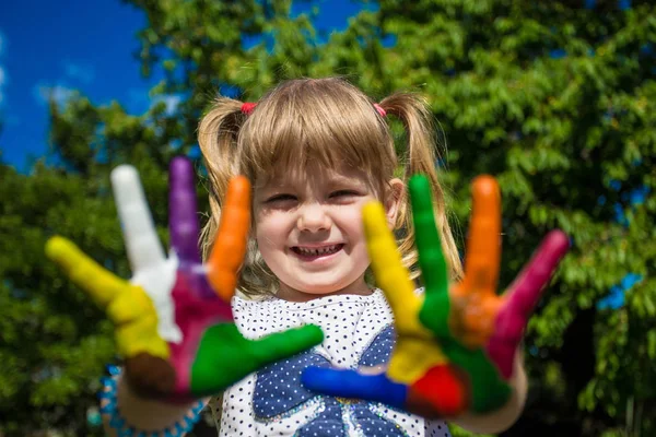 Schattig meisje toont haar handen geschilderd in heldere kleuren. Hand afdrukken. — Stockfoto