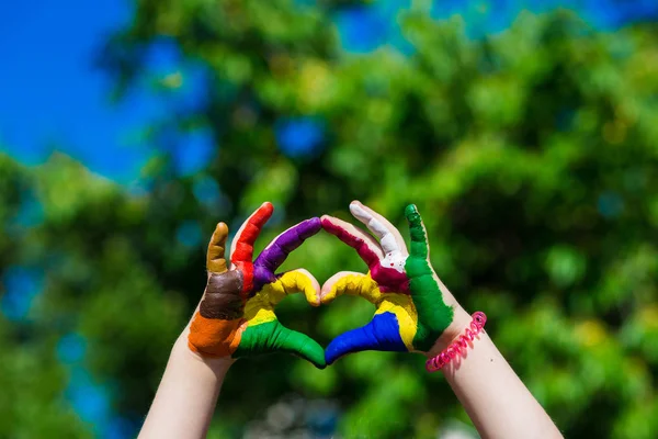 Les mains d'enfants peintes dans des couleurs vives font une forme de coeur sur fond de nature estivale — Photo