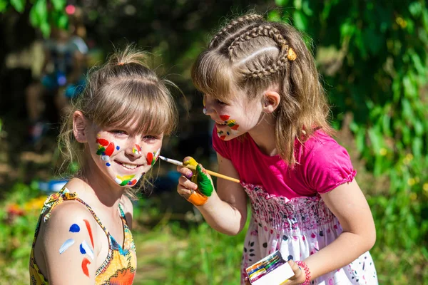 Les petites sœurs heureuses jouent avec les couleurs dans le parc, les enfants se peignent mutuellement — Photo