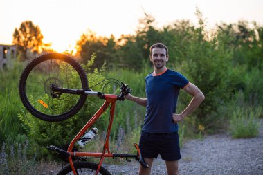 Sportif bir delikanlı bir bisiklet günbatımında tutuyor