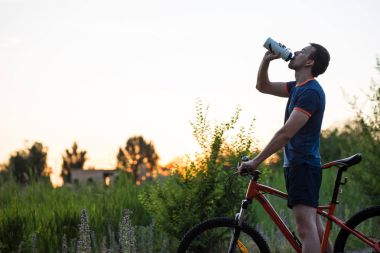 Bir bisiklet içme suyu spor şişeden günbatımında genç sportif kişini