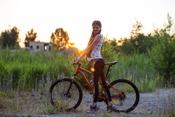 Atractiva chica deportiva con el pelo largo en una bicicleta en la puesta del sol —  Fotos de Stock