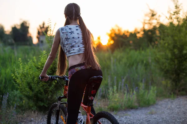 Attraktive sportliche Mädchen mit langen Haaren auf einem Fahrrad bei Sonnenuntergang — Stockfoto