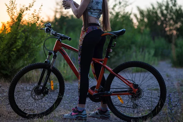 Menina desportiva atraente com cabelos longos em uma bicicleta no pôr do sol — Fotografia de Stock