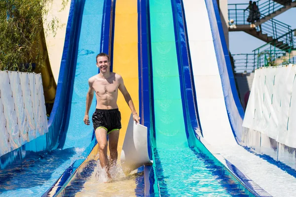 Vrolijke jongeman heeft plezier op vakantie op een dia in het waterpark — Stockfoto