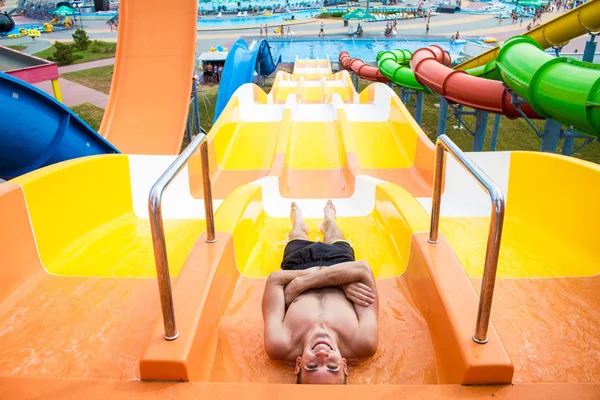 Vrolijke jongeman heeft plezier op vakantie op een dia in het waterpark — Stockfoto