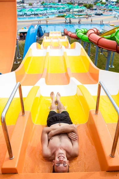 Młody, wesoły człowiek ma zabawy na wakacje na slajdzie w parku wodnego — Zdjęcie stockowe