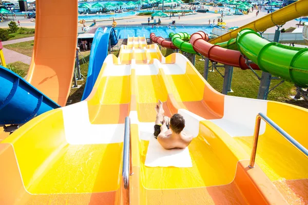 Vrolijke jongeman heeft plezier op vakantie op een dia in het waterpark — Stockfoto