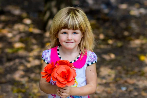 Porträtt av bedårande leende liten flicka med röda blommor i hennes händer — Stockfoto