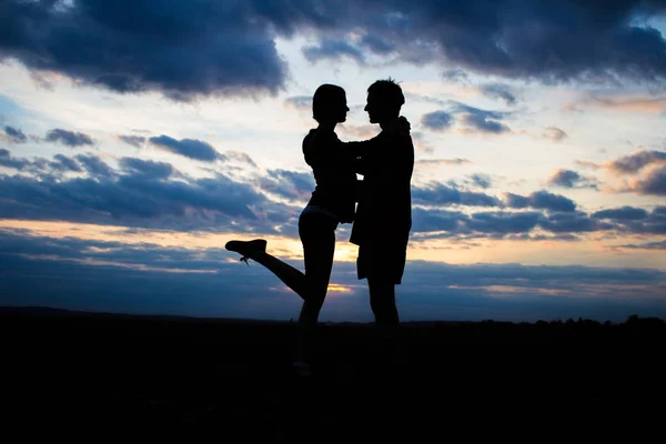 Silhueta lindo casal em um campo ao pôr do sol com um céu dramático — Fotografia de Stock