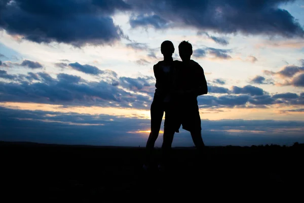 Silhueta lindo casal em um campo ao pôr do sol com um céu dramático — Fotografia de Stock