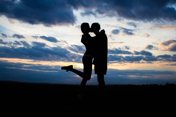 Silhouette bella coppia in un campo al tramonto con un cielo drammatico — Foto Stock