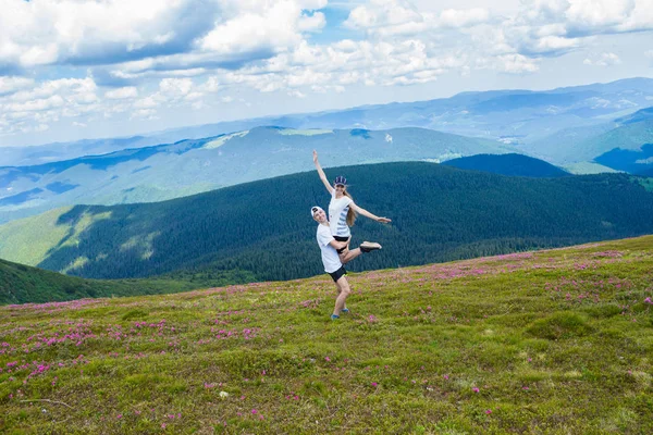 Un giovane uomo felice tiene una donna alta in montagna con un bel cielo sullo sfondo in una giornata estiva — Foto Stock