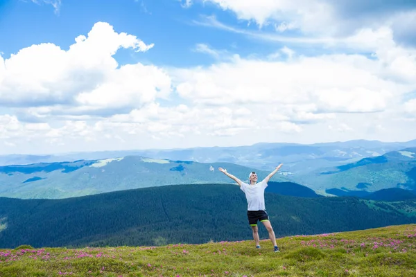 Letní turistiku v horách. Sání Asijské twink muž v čepici s rukama nahoru na vrcholu hory obdivuje povahu — Stock fotografie