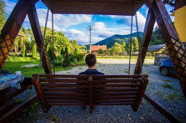 Genç bir adam bir salıncak düşünme üzerinde oturan ve dağlar seyir