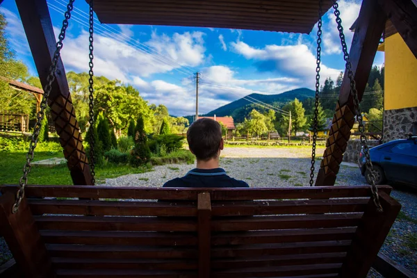 Genç bir adam bir salıncak düşünme üzerinde oturan ve dağlar seyir