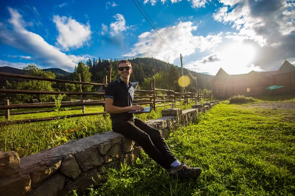 Genç adam dağlarda açık dizüstü bilgisayar çalışıyor