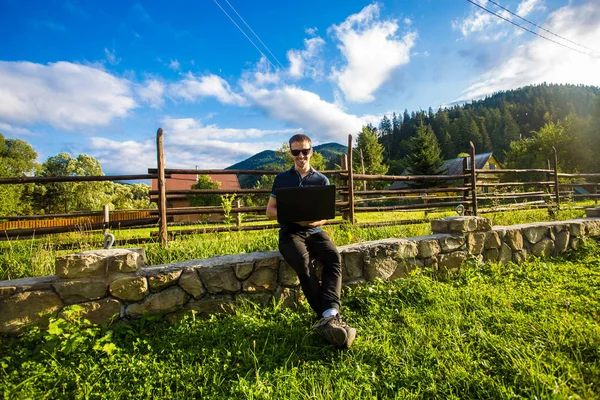 Genç adam dağlarda açık dizüstü bilgisayar çalışıyor