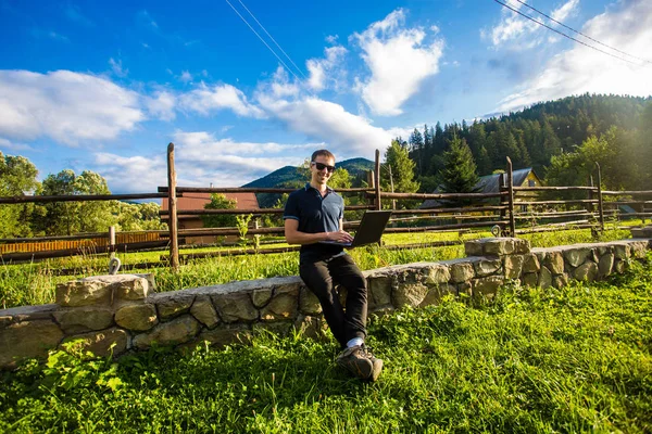 Genç adam dağlarda açık dizüstü bilgisayar çalışıyor